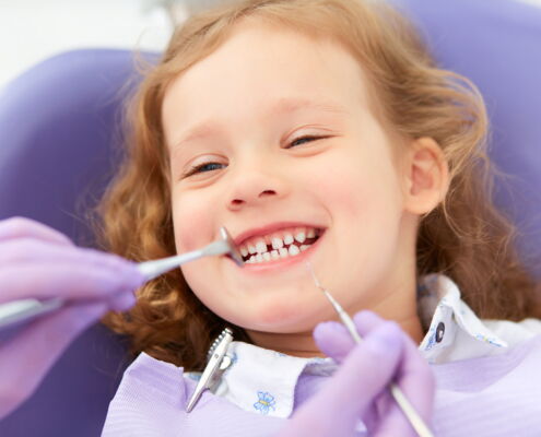 Lächelndes Kind mit Michzahngebiss sitzt auf Zahnarztstuhl und wird behandelt