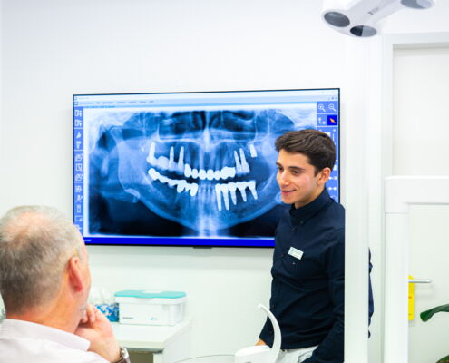 Zahnarzt und Patient blicken auf Wandmonitor mit Röntgenbild eines Gebisses
