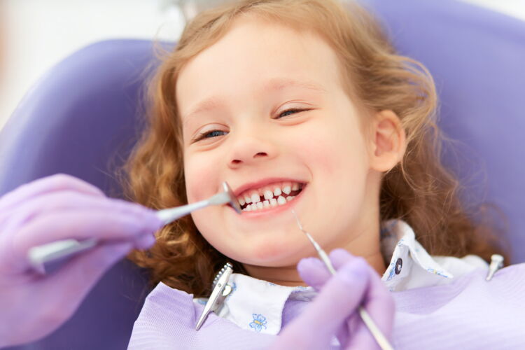 Lächelndes Kind mit Michzahngebiss sitzt auf Zahnarztstuhl und wird behandelt